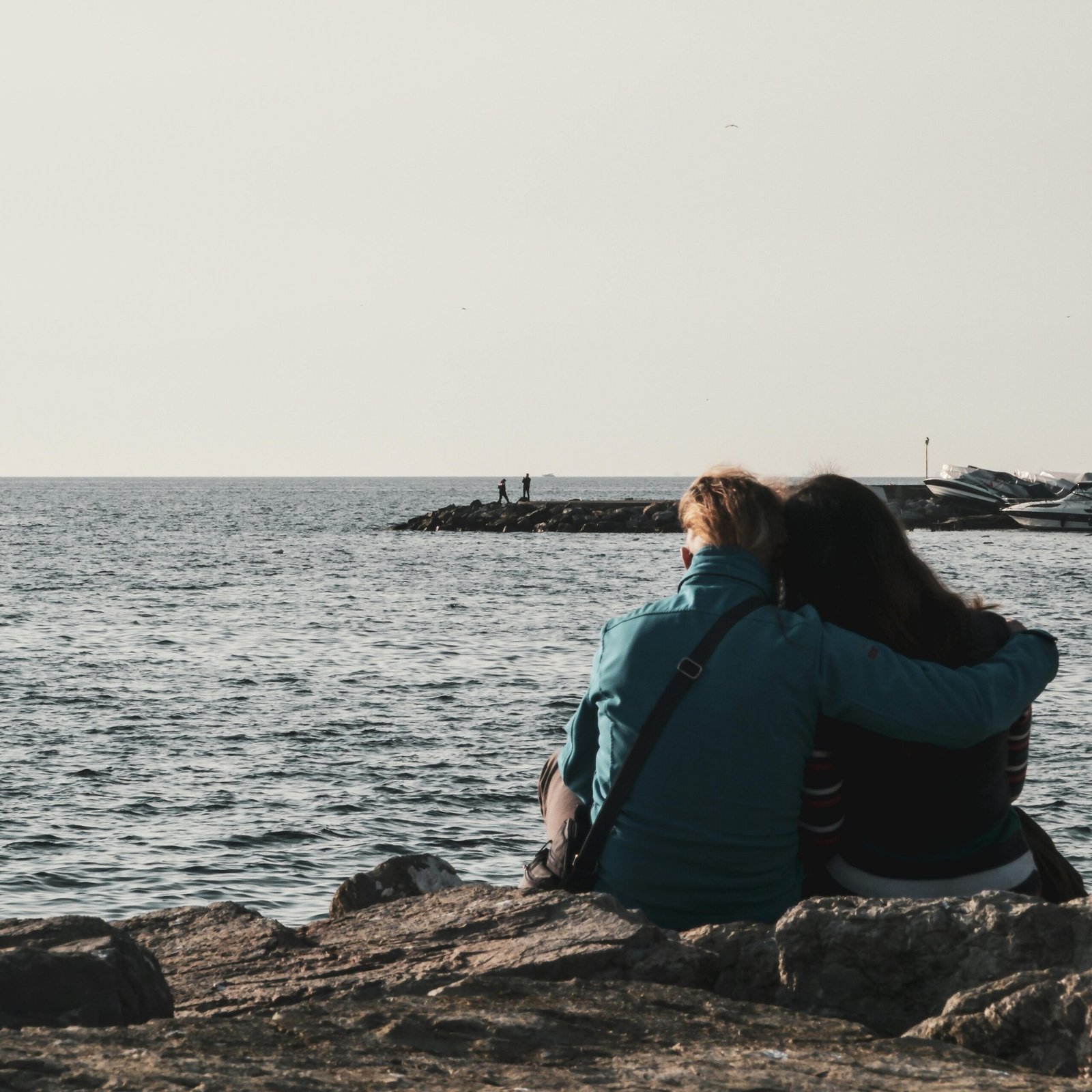 A couple shares a tender moment sitting on rocks by the sea during sunset.